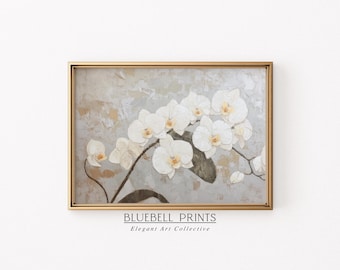 May include: A framed print of a white orchid flower with a textured background. The print is in a gold frame and has the text "BLUEBELL PRINTS Elegant Art Collective" at the bottom.