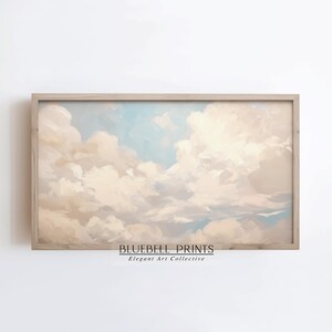 May include: A rectangular wall art print in a light wood frame featuring a painted sky with soft, voluminous cream and beige clouds against a pale blue background. The text BLUEBELL PRINTS Elegant Art Collective is printed in black at the bottom.