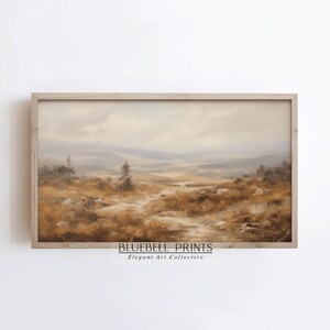 Può includere: Un dipinto di paesaggio in una cornice di legno chiaro che raffigura un vasto campo dai toni tenui con erbe color marrone dorato, rocce sparse e colline lontane sotto un cielo nuvoloso. Il testo BLUEBELL PRINTS Elegant Art Collective è stampato sotto.