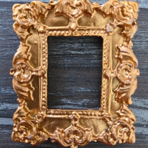 Puede incluir: Un marco de fotos de color dorado adornado con un diseño decorativo. El marco está vacío y listo para una foto o una obra de arte.