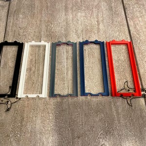 May include: Five rectangular frames arranged in a row, each featuring a thin border and small decorative tabs at the top and bottom. The frames are colored black, white, gray, dark blue, and red, all displaying a consistent, uniform design.