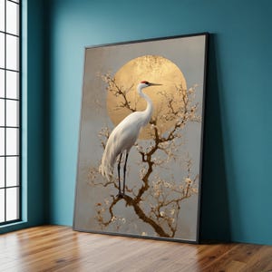 Könnte beinhalten: Gerahmter Kunstdruck mit einem weißen Kranich mit rotem Kopf, der auf einem blühenden Ast sitzt. Im Hintergrund befindet sich eine goldene Sonnenform. Das Kunstwerk hat eine neutrale Farbpalette mit einem Hauch von Gold, was eine ruhige und elegante Ästhetik schafft.