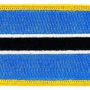 May include: A rectangular patch featuring the flag of Botswana. The flag has a light blue background with a horizontal black stripe in the center, bordered by white stripes. The patch is outlined with a yellow border.