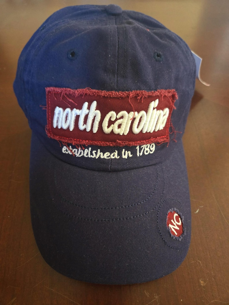 May include: Navy blue baseball cap with "north carolina" embroidered on a burgundy patch. The text "established in 1789" is below the patch. A small "NC" patch is on the side.