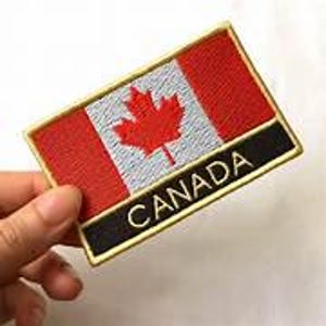 Könnte beinhalten: Gestickter Aufnäher mit der kanadischen Flagge. Der rechteckige Aufnäher hat einen roten Hintergrund mit einem weißen Quadrat und einem roten Ahornblatt in der Mitte. Das Wort "CANADA" ist in Weiß auf einem schwarzen Balken gestickt.