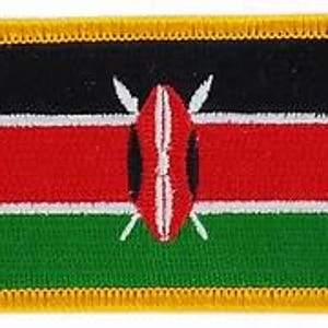 May include: Rectangular patch depicting the Kenyan flag. The top is black, with a red stripe below, and a green stripe at the bottom. A white shield and spears are in the centre of the red stripe. The patch has a gold border.