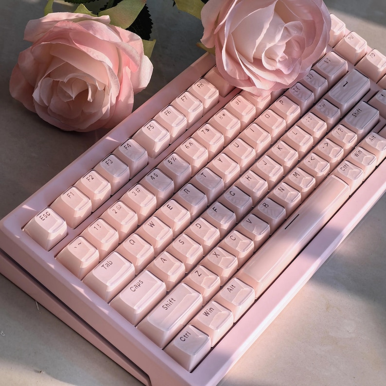 Op de afbeelding: Een roze mechanisch toetsenbord met witte toetsen en zwarte letters. Het toetsenbord heeft een rij met functietoetsen, een nummerrij, een letterrij en een onderste rij met toetsen voor control, shift, win, alt en spatie.