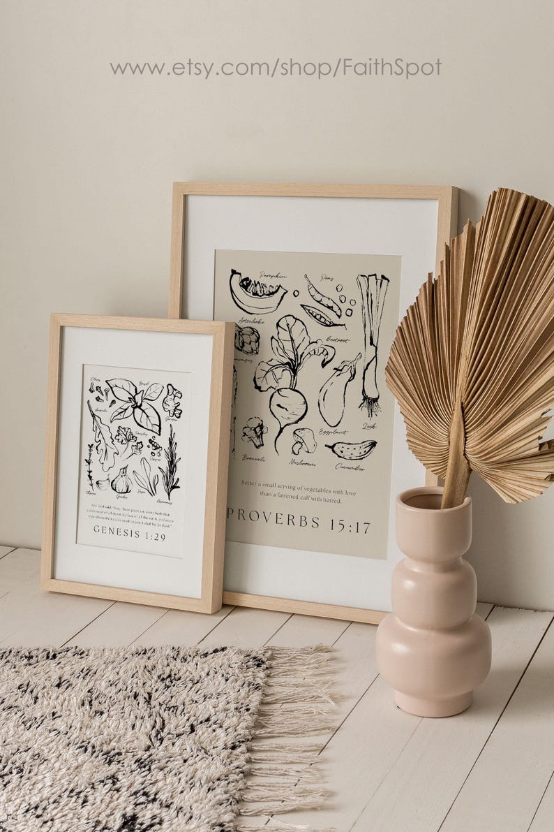 Op de afbeelding: Twee ingelijste kunstdrukken met botanische illustraties en tekst, &eacute;&eacute;n met Genesis 1:29 en de andere met Spreuken 15:17. Een roze vaas bevat een gedroogd palmblad. De achtergrond is een lichtbeige muur en een getextureerd tapijt.
