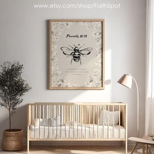 Pu&ograve; includere: Una stampa incorniciata con un'illustrazione di un'ape in bianco e nero e il testo "Proverbi 16:24". La stampa &egrave; circondata da un bordo floreale e appesa sopra una culla di legno. Un piccolo albero in un cesto intrecciato &egrave; a sinistra.