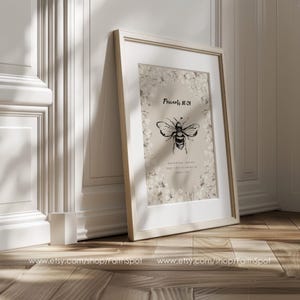 Pu&ograve; includere: Una stampa incorniciata con un'illustrazione di un'ape in bianco e nero e il testo "Proverbi 16:24". L'opera &egrave; incorniciata in bianco, con un bordo floreale. La cornice &egrave; appoggiata a un muro.