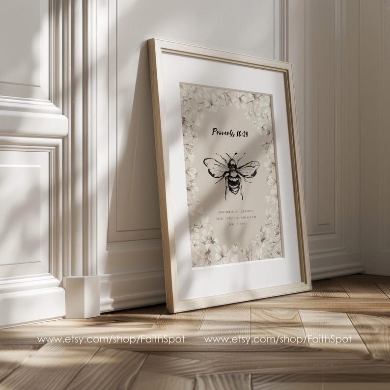 Pu&ograve; includere: Una stampa incorniciata con un'illustrazione di un'ape in bianco e nero e il testo "Proverbi 16:24". L'opera &egrave; incorniciata in bianco, con un bordo floreale. La cornice &egrave; appoggiata a un muro.
