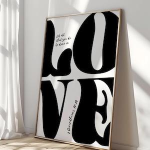 May include: Black and white typography print with the word "LOVE" in large, bold letters. The text "Let all that you do be done in love" is written above the word "LOVE". The text "1 Corinthians 16:14" is written below the word "LOVE".