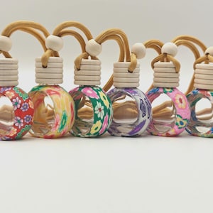 May include: Six decorative car air fresheners with floral designs. Each has a wooden cap, a beige cord, and a wooden bead. The air fresheners are in red, yellow, green, purple, pink, and blue.