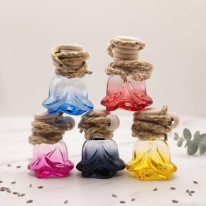 May include: Five small glass bottles shaped like flower buds in blue, red, pink, dark blue, and yellow. Each bottle features a wooden cap secured with a thick, gold-flecked jute rope tied around the neck, creating a decorative hanging display.