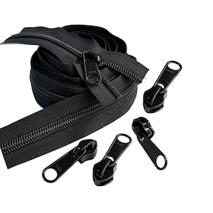 May include: A roll of black zipper tape with four black zipper pulls. The zipper tape is coiled and the zipper pulls are scattered around the tape.
