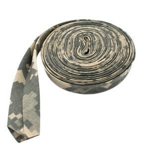May include: A roll of camouflage-patterned fabric ribbon. The ribbon is rolled up in a spiral shape and has a tan and green color scheme.
