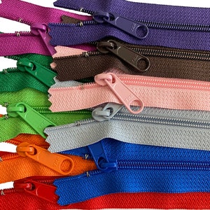 May include: Assortment of zipper closures in various colors, including red, orange, blue, green, purple, brown, pink, and gray. The zippers are arranged in a stack, with the top zipper being red and the bottom zipper being gray.