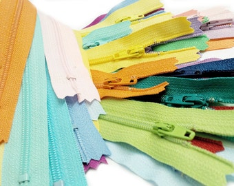 Puede incluir: Una colección de cintas de cremallera de colores en varios tonos pastel, incluyendo azul claro, verde, amarillo, naranja y morado. Las cremalleras están dispuestas en forma de abanico, mostrando los diferentes colores y texturas.