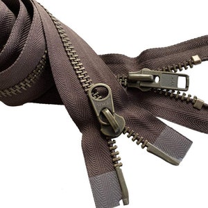 May include: Close-up of a brown zipper with a metal pull and teeth. The zipper is partially open, revealing the teeth and the fabric tape. The zipper is a YKK brand.