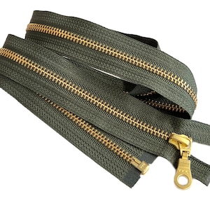 Könnte beinhalten: Nahaufnahme eines grünen Reißverschlusses mit einem goldenen Metall-Schieber. Der Reißverschluss ist von YKK und ist eine beliebte Wahl für Kleidung und Taschen.