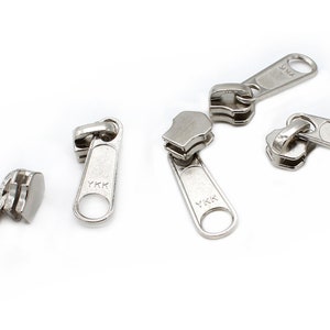 May include: Five silver zipper pulls with the YKK logo. The zipper pulls are isolated on a white background.