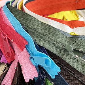 May include: A collection of colorful zippers in various shades, including red, blue, green, and orange. The zippers are arranged in a close-up shot, showcasing their different colors and styles. The image highlights the variety of zipper types available.