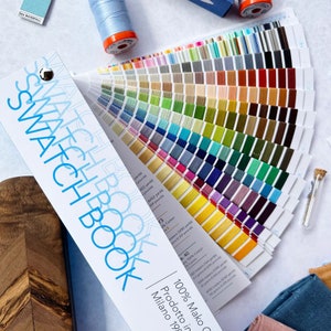 May include: A fan of colourful thread spools in a swatch book. The book is labelled "Swatch Book" and "100% Mako Cotton" with the text "Prodotto in Milano" and "100% Mako Cotton".
