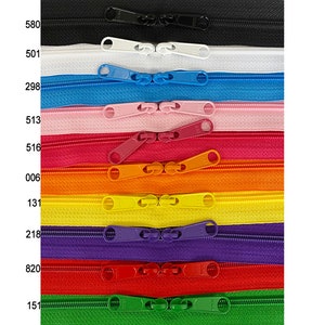 Puede incluir: Una selección de 10 tiradores de cremallera en varios colores, incluyendo negro, blanco, azul, rosa, rojo, naranja, amarillo, morado, verde y rojo. Los tiradores de cremallera están dispuestos verticalmente en una fila, con el color de cada tirador etiquetado con un número.