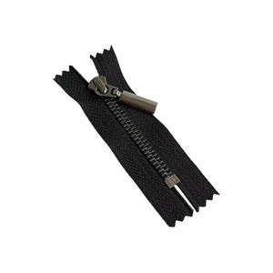 May include: A black zipper with a silver-colored pull tab and teeth. The zipper is open, revealing the teeth and the fabric tape. The zipper is angled diagonally against a white background.