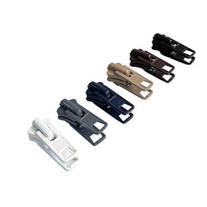 May include: A set of six zipper pulls in various colors, including white, gray, navy blue, brown, beige, and black. The zipper pulls are made of metal and have a simple, functional design.