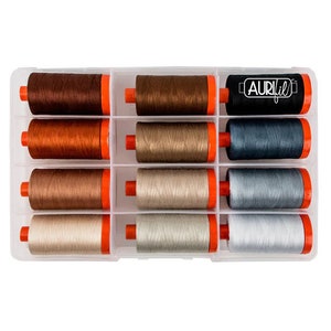 May include: A clear plastic storage box with 12 spools of thread. The spools are arranged in three rows of four. The spools are in shades of brown, beige, and gray. The box has a label that says "Aurifil".