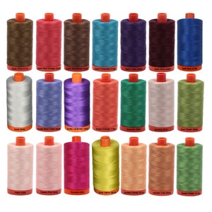 May include: A collection of 22 spools of thread in various colors, including dark olive, dark red orange, dark sandstone, dark turquoise, dark violet, dark wine, delft blue, dove, dusty blue violet, dusty lavender, dusty orange, emerald, emine, farm green, flesh, fleshy pink, fuchsia, gold yellow, golden honey, golden toast, and grass green. Each spool has a white label with the color name and number.