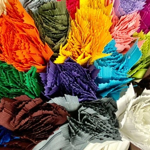 May include: A collection of colorful fabric scraps, each cut into a unique shape and texture. The scraps are arranged in a bouquet-like formation, showcasing a variety of colors, including orange, green, purple, blue, and white.