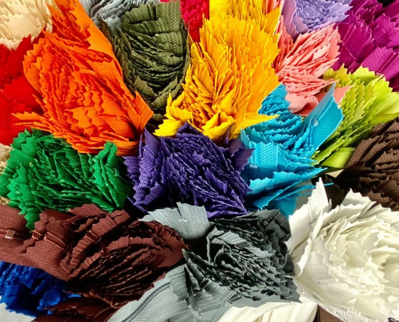 May include: A collection of colorful fabric scraps, each cut into a unique shape and texture. The scraps are arranged in a bouquet-like formation, showcasing a variety of colors, including orange, green, purple, blue, and white.