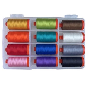 Pode incluir: Uma caixa de armazenamento de plástico transparente com 12 carretéis de fio. Os carretéis estão dispostos em três filas de quatro. Os carretéis são de várias cores, incluindo dourado, verde, castanho, laranja, vermelho, rosa, roxo, azul, turquesa, branco, cinzento e preto.