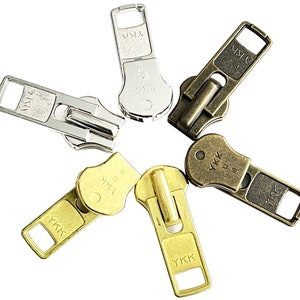 May include: Six different zipper pulls in various finishes, including silver, gold, and antique brass. Each pull features the YKK logo and is designed for use with zippers.