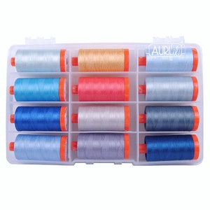 May include: A clear plastic storage box with 12 spools of thread. The spools are in various shades of blue, gray, and red. The box has the word "Aurifil" printed on the side.