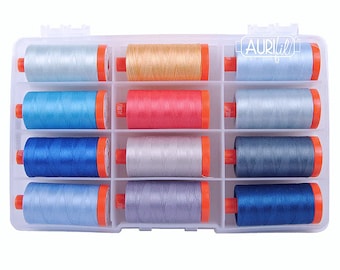 May include: A clear plastic storage box with 12 spools of thread. The spools are in various shades of blue, gray, and red. The box has the word "Aurifil" printed on the side.