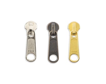May include: Three metal zipper pulls in silver, black, and gold. Each pull has the word "YKK" engraved on the front.