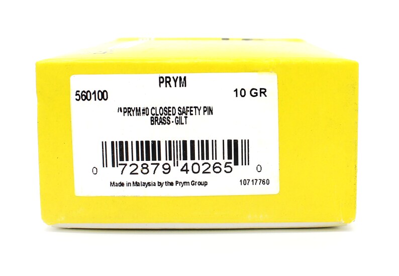 May include: A yellow box with a white label that reads "PRYM #0 CLOSED SAFETY PIN BRASS-GILT" and a barcode. The box also has the text "560100", "10 GR", "Made in Malaysia by the Prym Group", and "10717760".