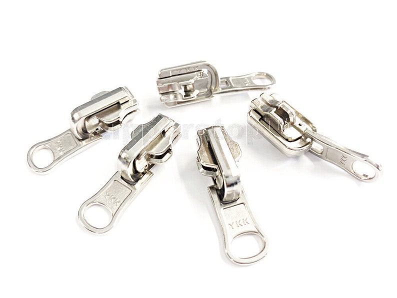 May include: Five silver zipper pulls with a YKK logo. The zipper pulls are arranged in a circular pattern on a white background.