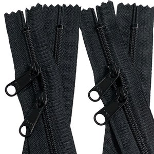 May include: Close-up of several black zippers with double pulls. The zippers are made of a black fabric with a textured surface and have black metal pulls. The pulls have a rounded shape with a hole for easy gripping.