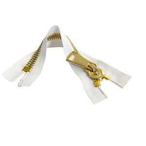 Op de afbeelding: Een witte rits met een gouden metalen schuif en treklip. De rits is open en de tanden zijn zichtbaar.
