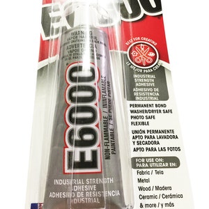 Może przedstawiać: Srebrna tubka kleju przemysłowego E6000 o wysokiej wytrzymałości z czerwoną i białą etykietą. Etykieta zawiera napis "Niepalny/Ininflammable, Malowalny/Se puede pintar" oraz "Klejenie o wysokiej wytrzymałości przemysłowej/Adhesivo de Resistencia Industrial". Etykieta zawiera również listę zastosowań kleju, w tym tkanina, metal, drewno, ceramika i wiele innych.