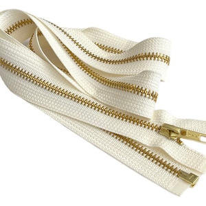 May include: A close-up of a white zipper with gold metal teeth. The zipper is folded in half and the ends are visible.