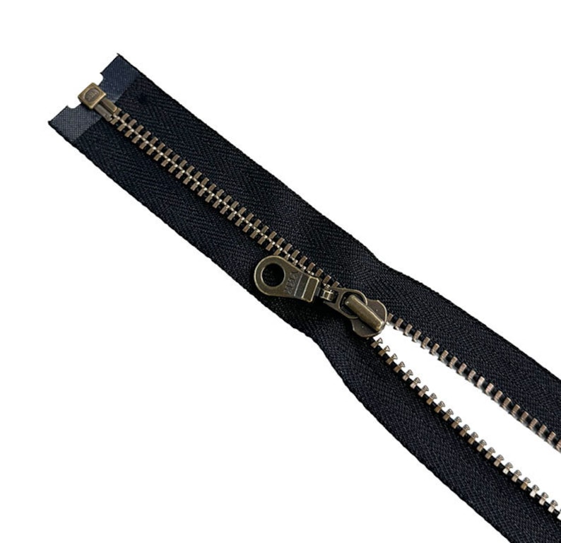 May include: A black zipper with a brass slider and pull. The zipper is open and the teeth are visible.