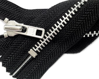 May include: A black zipper with a silver metal slider and teeth. The zipper is folded in half and the slider is in the middle of the zipper.