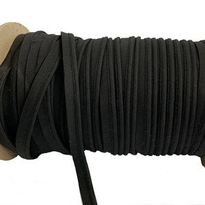 May include: A spool of black cotton cord, wound around a cardboard core. The cord is approximately 6mm wide and has a smooth, slightly textured surface.
