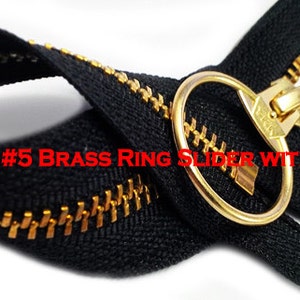 May include: A black zipper with a gold brass ring slider and lock. The zipper is labeled "YKK #5 Brass Ring Slider with Lock".