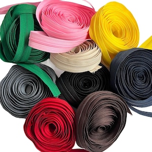 May include: Assortment of zipper tape in various colors, including pink, yellow, green, black, brown, and beige. The zipper tape is rolled up and ready to be used for sewing projects.